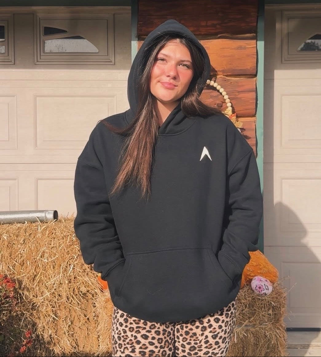 Person wearing a black hoodie with EXALT logo, standing in front of a wooden building.